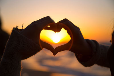 Cropped hands making heart shape at sunset