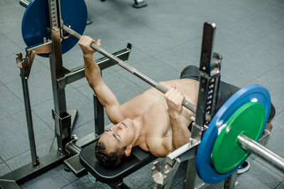 Shirtless athlete doing weightlifiting at bench press in gym