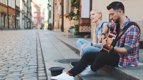 Young couple sitting on sidewalk in city