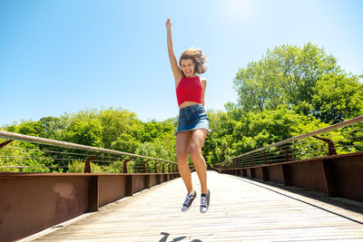 Cheerful girl jumping on footbridge against sky