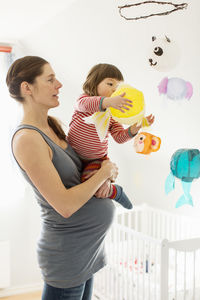 Pregnant woman carrying girl playing with toy in baby room