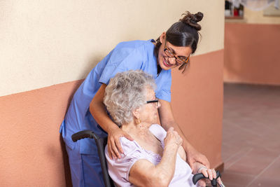 Happy senior woman with walking stick in wheelchair with her caregiver at home.