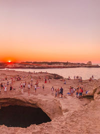 People at beach against clear sky during sunset