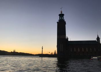 Silhouette of building by sea against sky during sunset