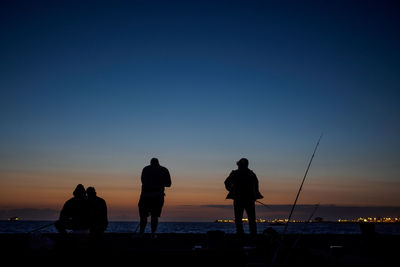 Silhouette people enjoying at beach against blue sky during sunset