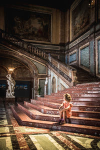 Full length of girl sitting on staircase in palace