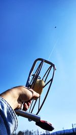 Cropped hand of man holding kite string against clear blue sky