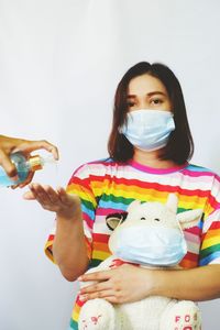 Portrait of a woman wearing a mask  standing up to pick up the alcohol gel against white background