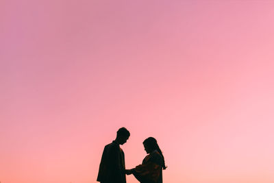 Man and woman standing against pink sky during sunset