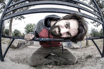 Close-up portrait of young man looking through bench at park