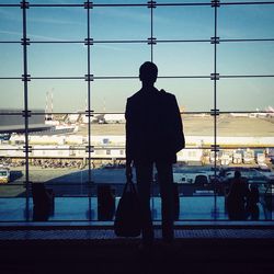 Rear view of silhouette man standing against glass at airport