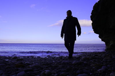 Silhouette man standing at beach against clear sky during sunset