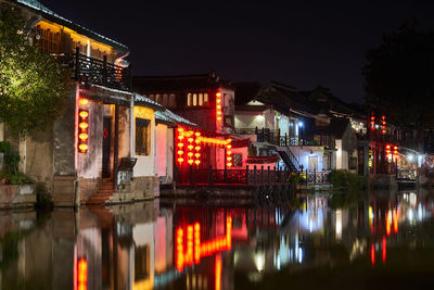 Illuminated buildings by river against sky at night