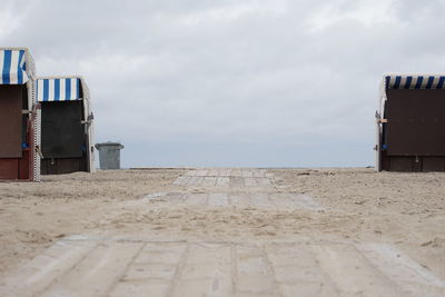 Hooded beach chairs on sand against sky