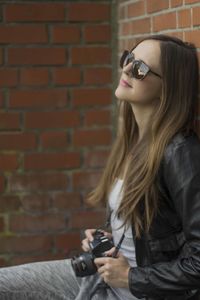 Beautiful woman with camera leaning on brick wall