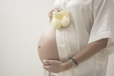 Midsection of pregnant woman standing against white background