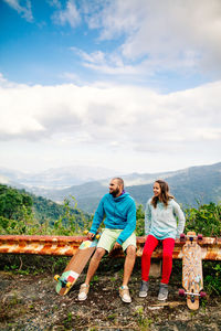 Couple sitting on railing against sky