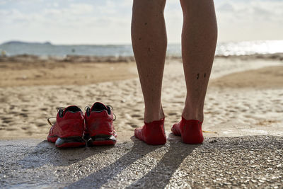 Legs of man by sports shoes at beach