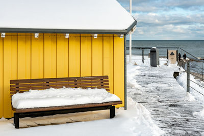 Snow covered land by sea against sky