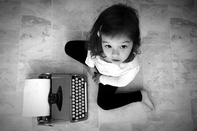High angle view of girl with typewriter sitting on floor at home