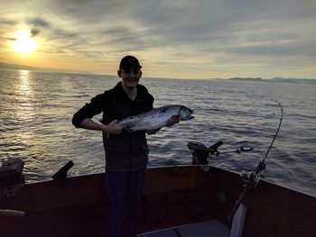 Man fishing in sea against sunset sky