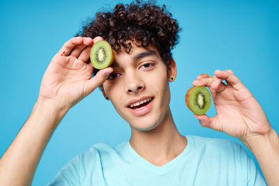 Portrait of young man holding apple against blue background