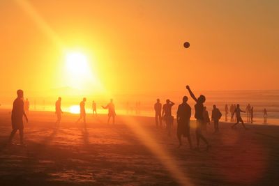 Silhouette people playing with ball on beach during sunset