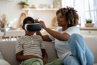 African american modern mom helping little boy son to put on virtual reality headset