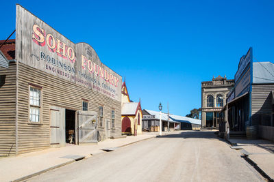 Road amidst buildings against clear blue sky