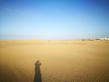 Shadow of man on sand in desert against clear blue sky