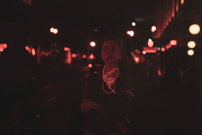 Full length portrait of woman standing against illuminated lights at night