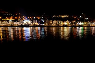 Illuminated cityscape by river against sky at night