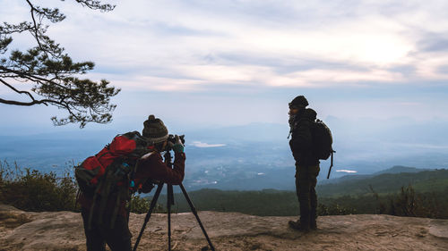 Man photographing woman with camera against sky