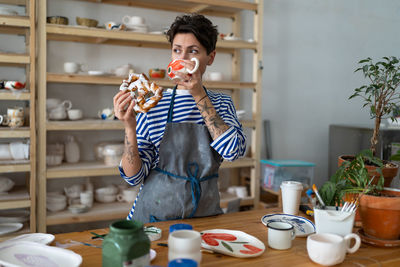 Italian young female owner in pottery workshop has coffee break, successful small business concept