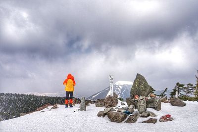 Rear view of man standing on snow covered mountain against sky