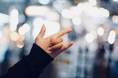 Close-up of woman showing horn sign against illuminated lights at night