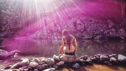 Rear view of shirtless woman on rock