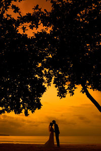 Silhouette man standing by tree against orange sky