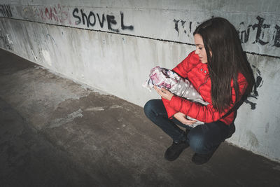 Young woman crouching with paper currency against wall