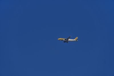 Low angle view of airplane flying against clear blue sky