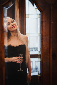 Portrait of young woman standing against window