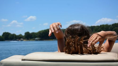 Rear view of woman relaxing on lounge chair by sea