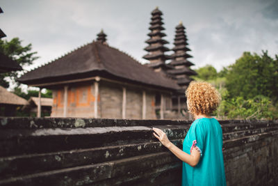 Rear view of woman standing by building against sky