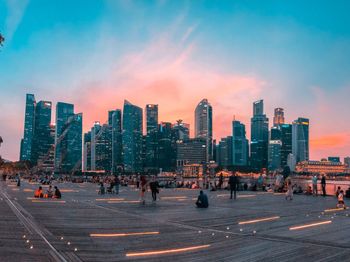 People relaxing at promenade in city against sky during sunset