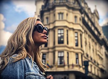 Close-up of mature woman wearing sunglasses against building in city