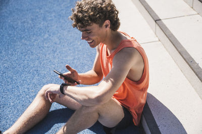 Happy sportsman using smart phone sitting in front of steps