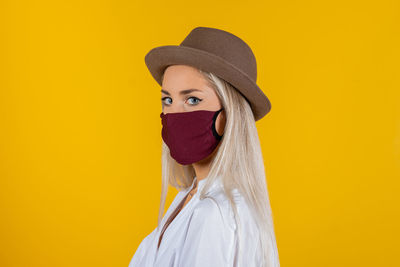Portrait of young woman wearing mask and hat against yellow background
