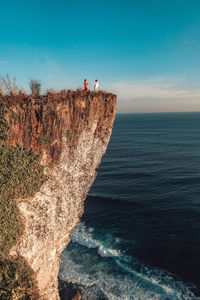 People on rock by sea against sky