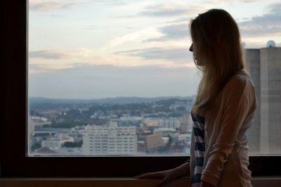 Woman looking at view while standing by window at home