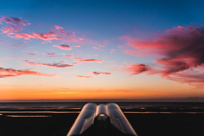 Telescope at beach against sky during sunset